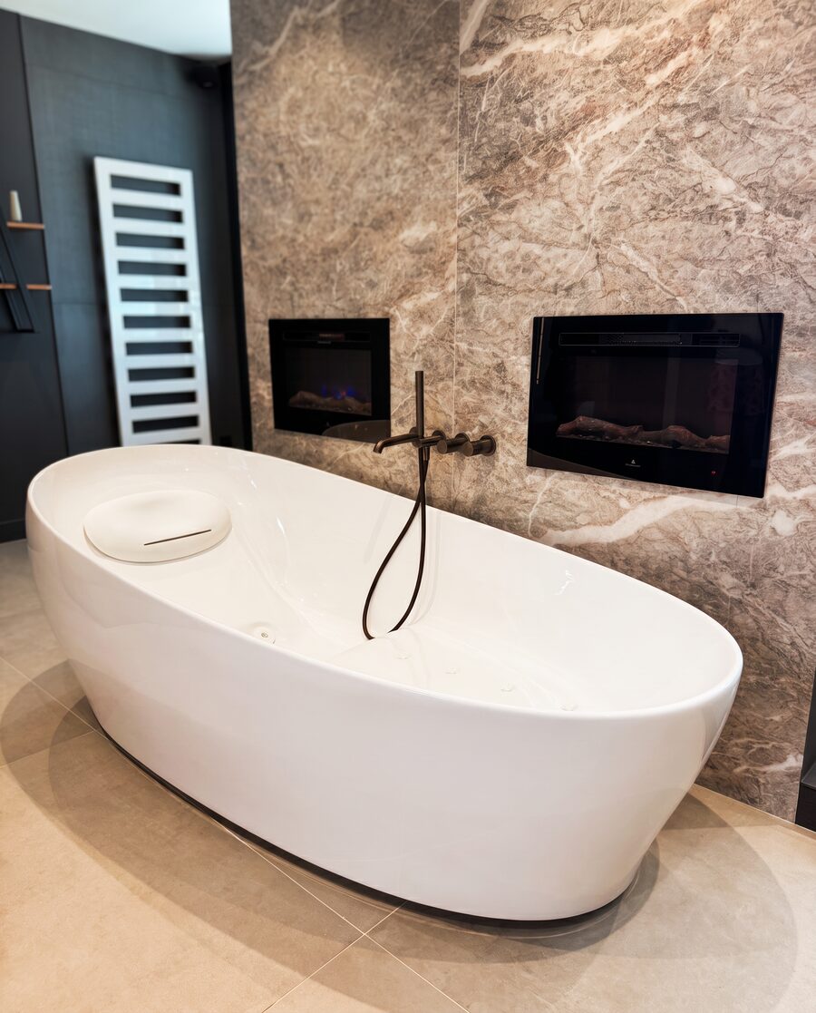 Freistehende Badewanne vor Marmorwand mit wandmontierter Armatur